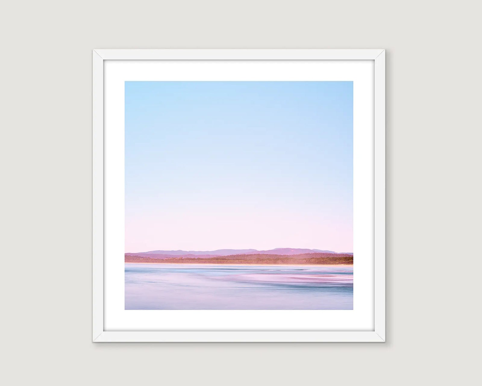 Framed landscape photograph of an ocean with mountains in the background and a blue sky.