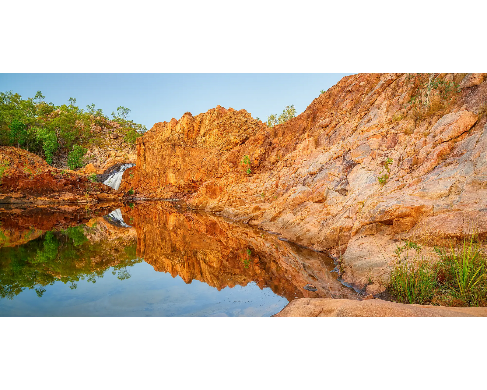 Rocky landscape with water reflection and Edith Falls in the background.
