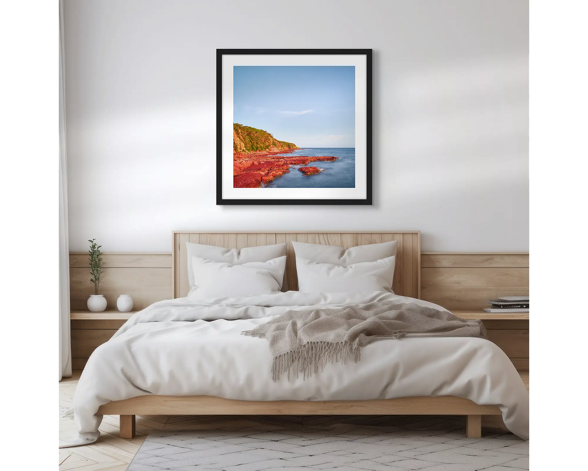 Point. Square, Merimbula wall art print with a black frame hung above a bed. 
