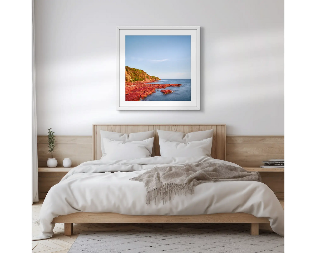 Point. Square, Merimbula wall art print with a white frame hung above a bed. 
