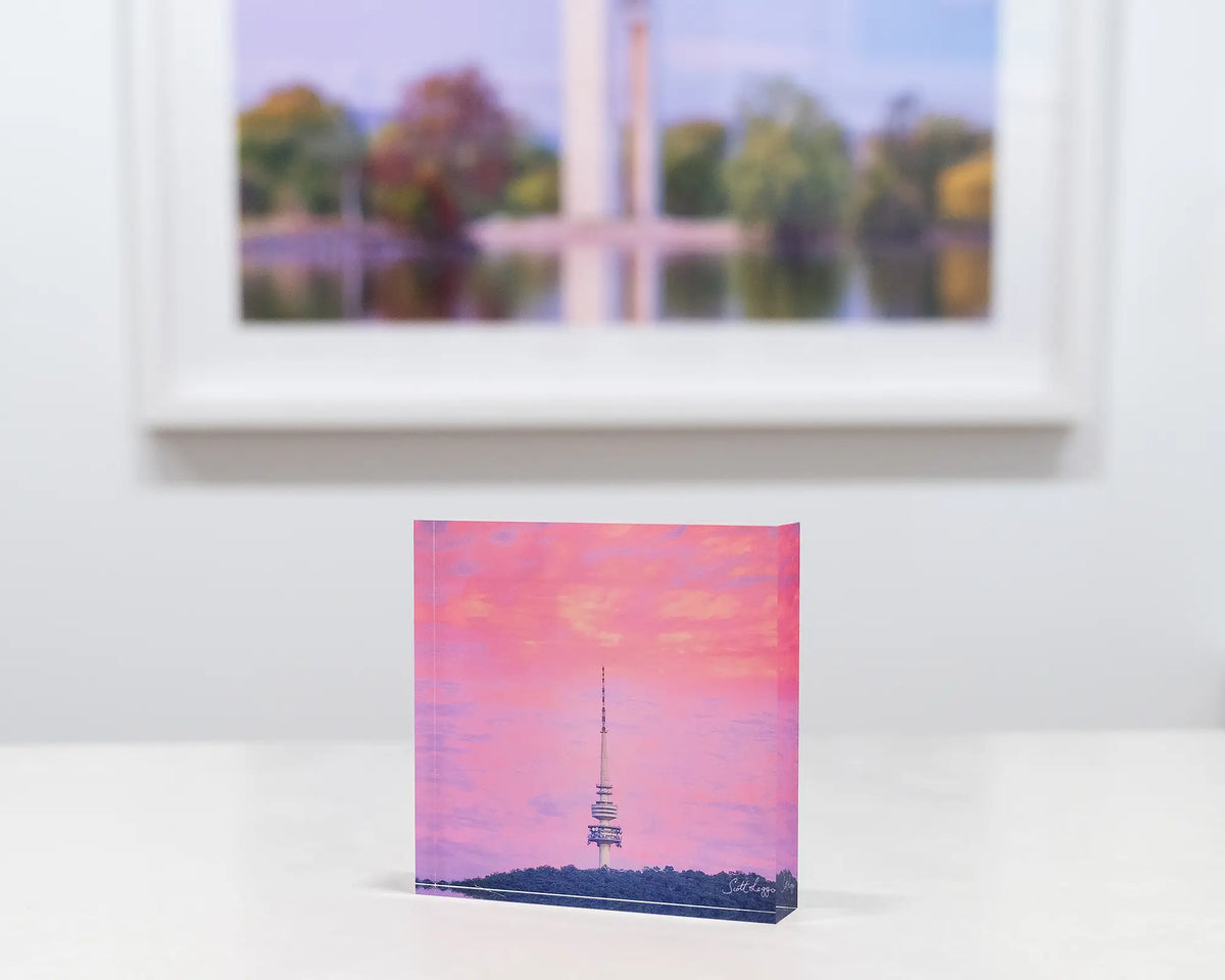 Pointer. Acrylic block of sunrise at Black Mountain Tower, on desk with Canberra artwork in background.