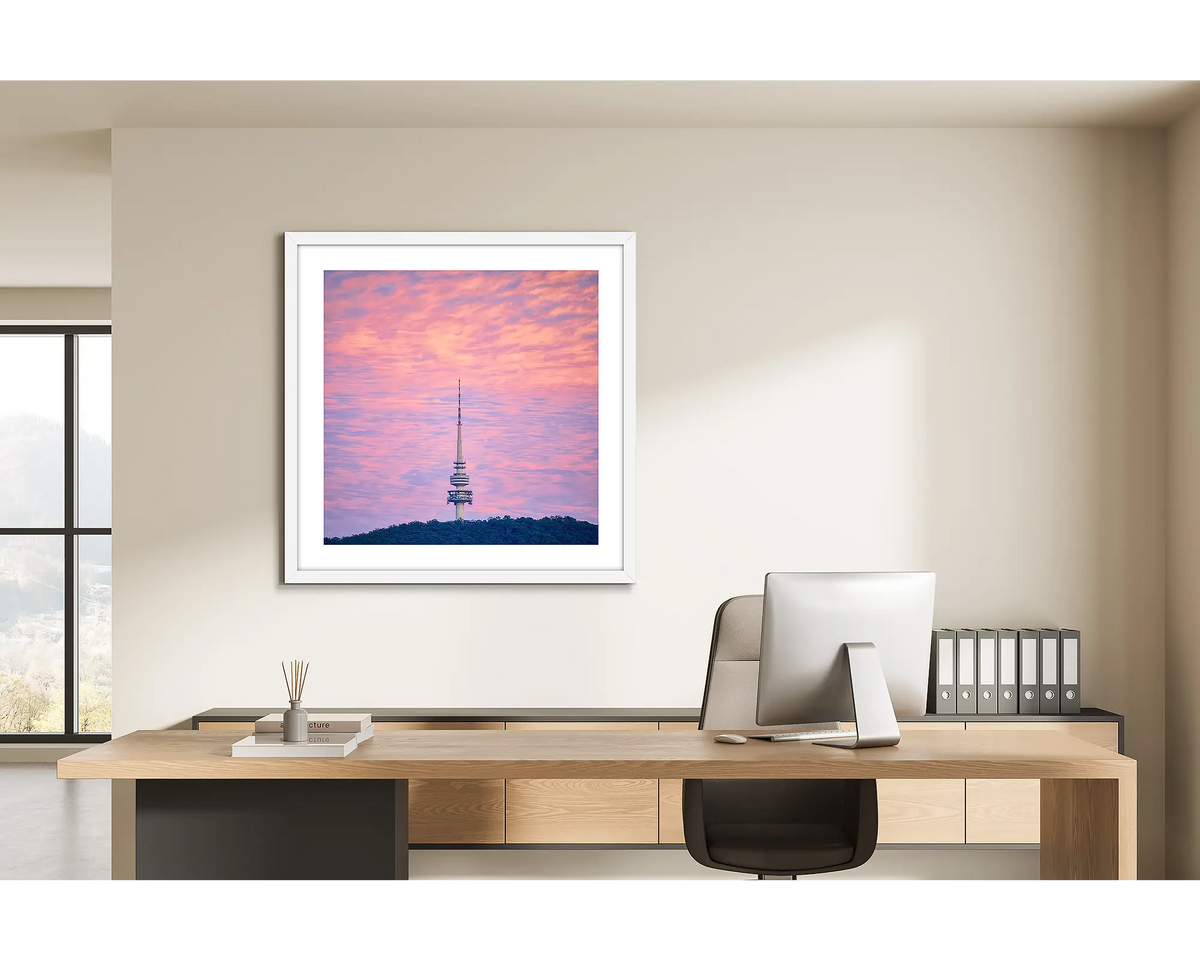 Pointer. Framed wall art print of a Telstra Tower at sunrise, with a white frame, hung in a light filled office. 