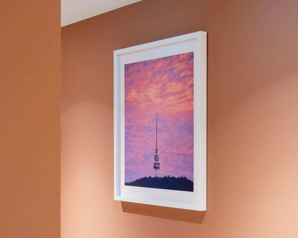 Pointer. Sunrise at Telstra Tower Canberra, with white frame hung on terracotta coloured wall in commercial space.