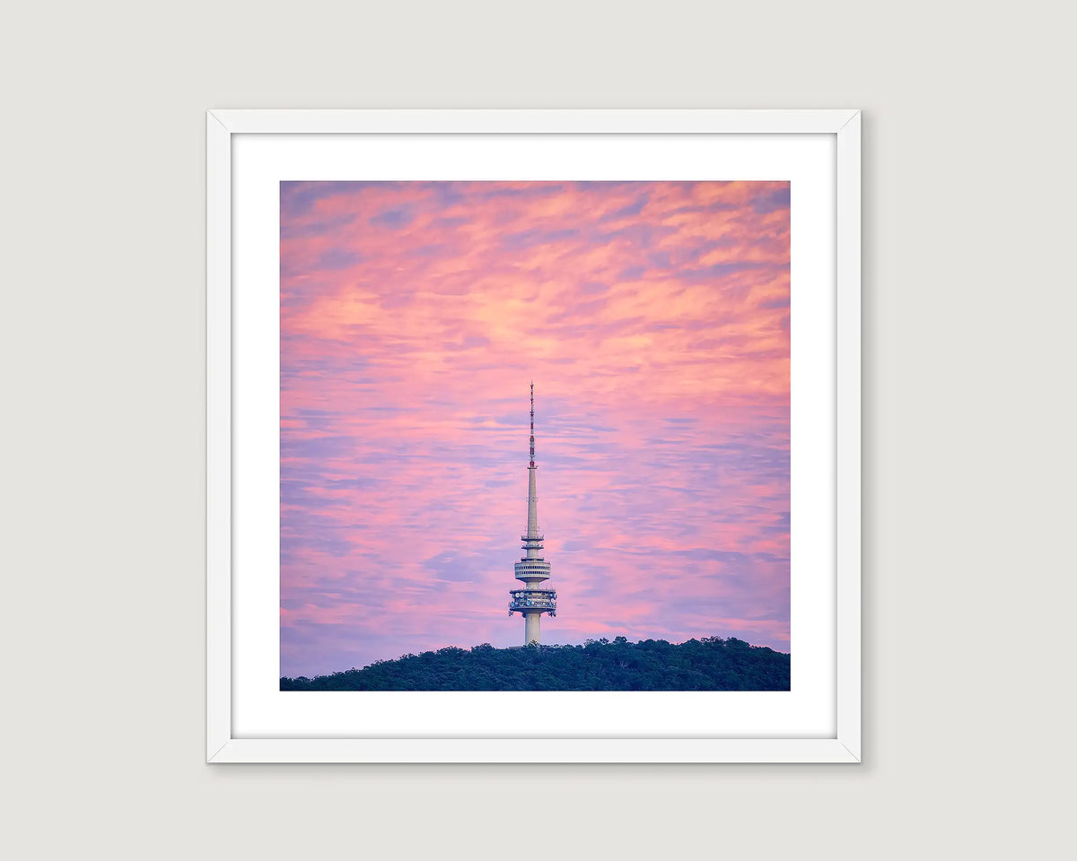 Framed photograph of a tower on a mountain with a pink cloudy sky.