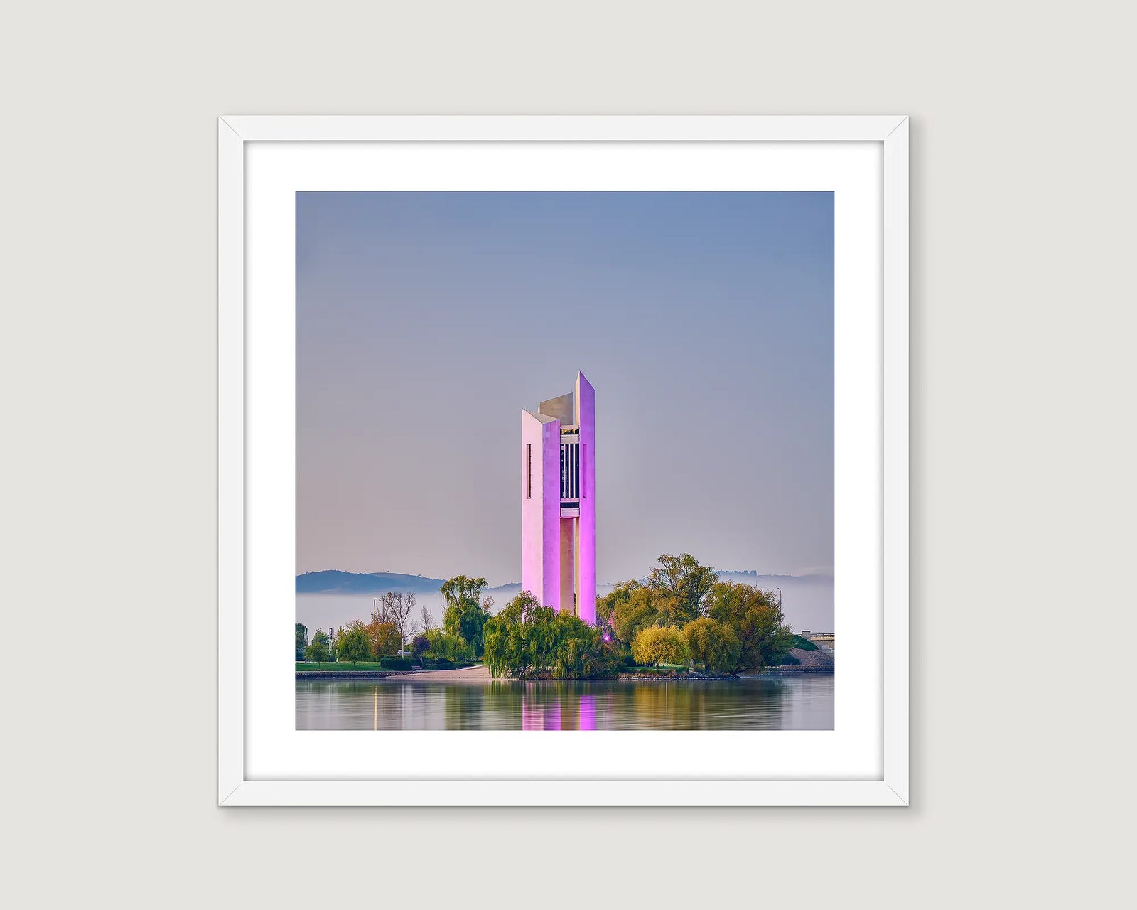 Framed photograph of the Carillon lit up in purple on a lake with fog and mountains and a blue sky.