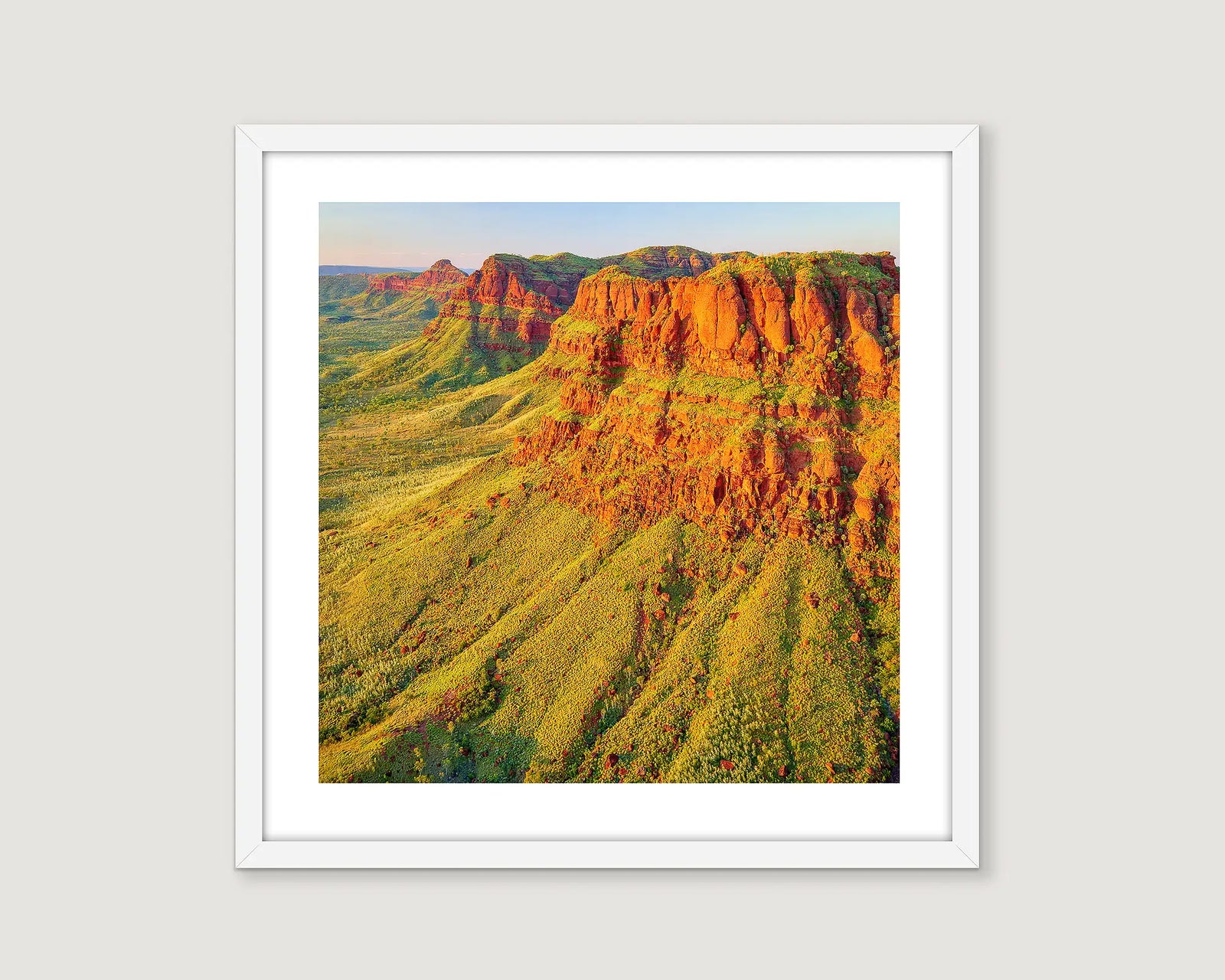 Framed landscape photograph of a red rock cliff with trees and a blue sky at the Kimberley.