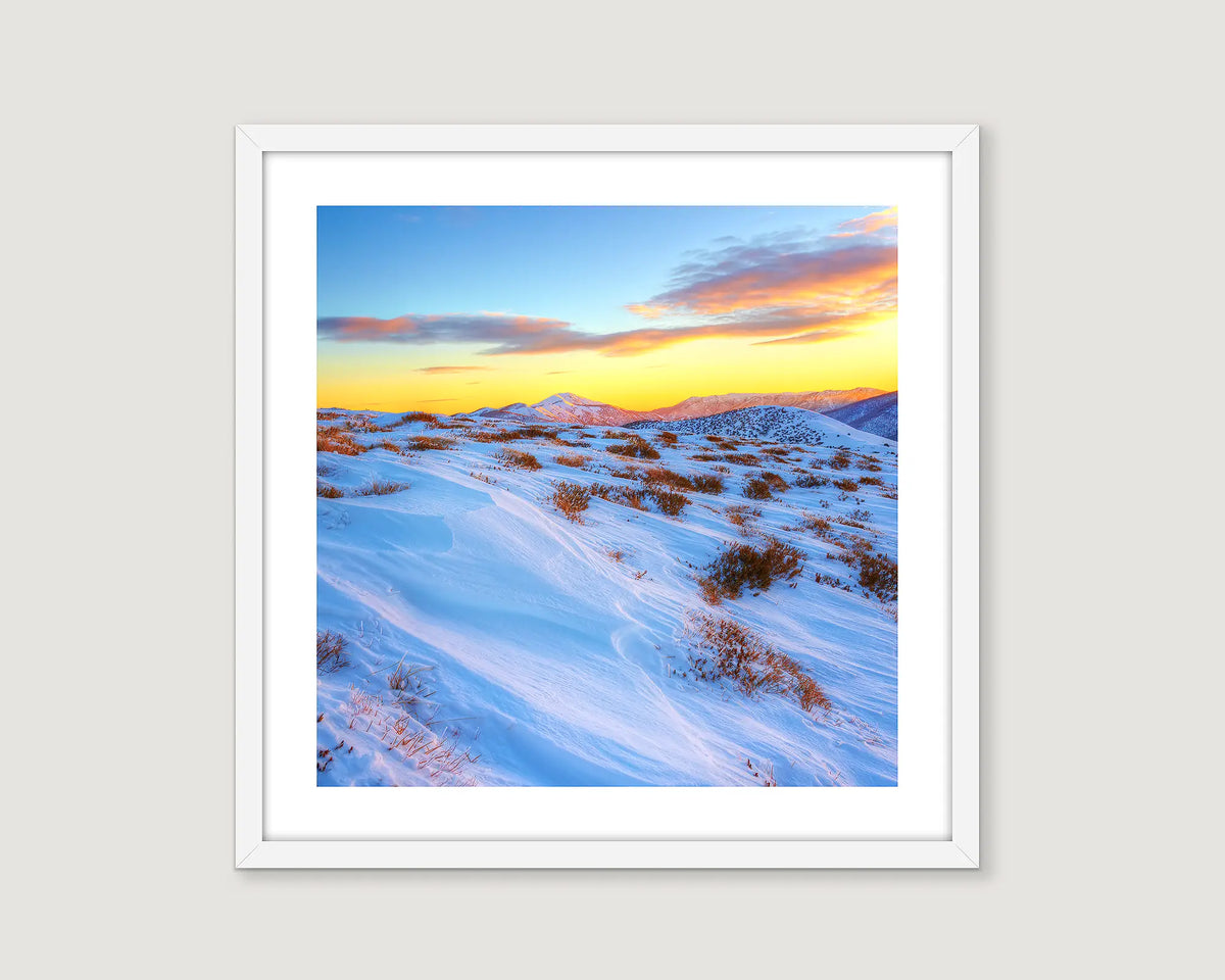 Framed landscape photograph of snow fields with a yellow sunrise and blue sky.
