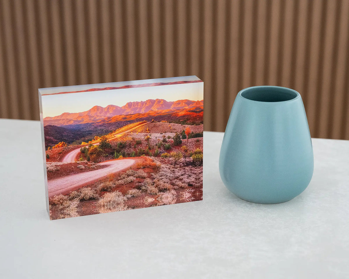 Razorback Ridge. Acrylic block of sunrise over Bunyeroo Valley and Wilpena Pound, on desk styled with a small vase.