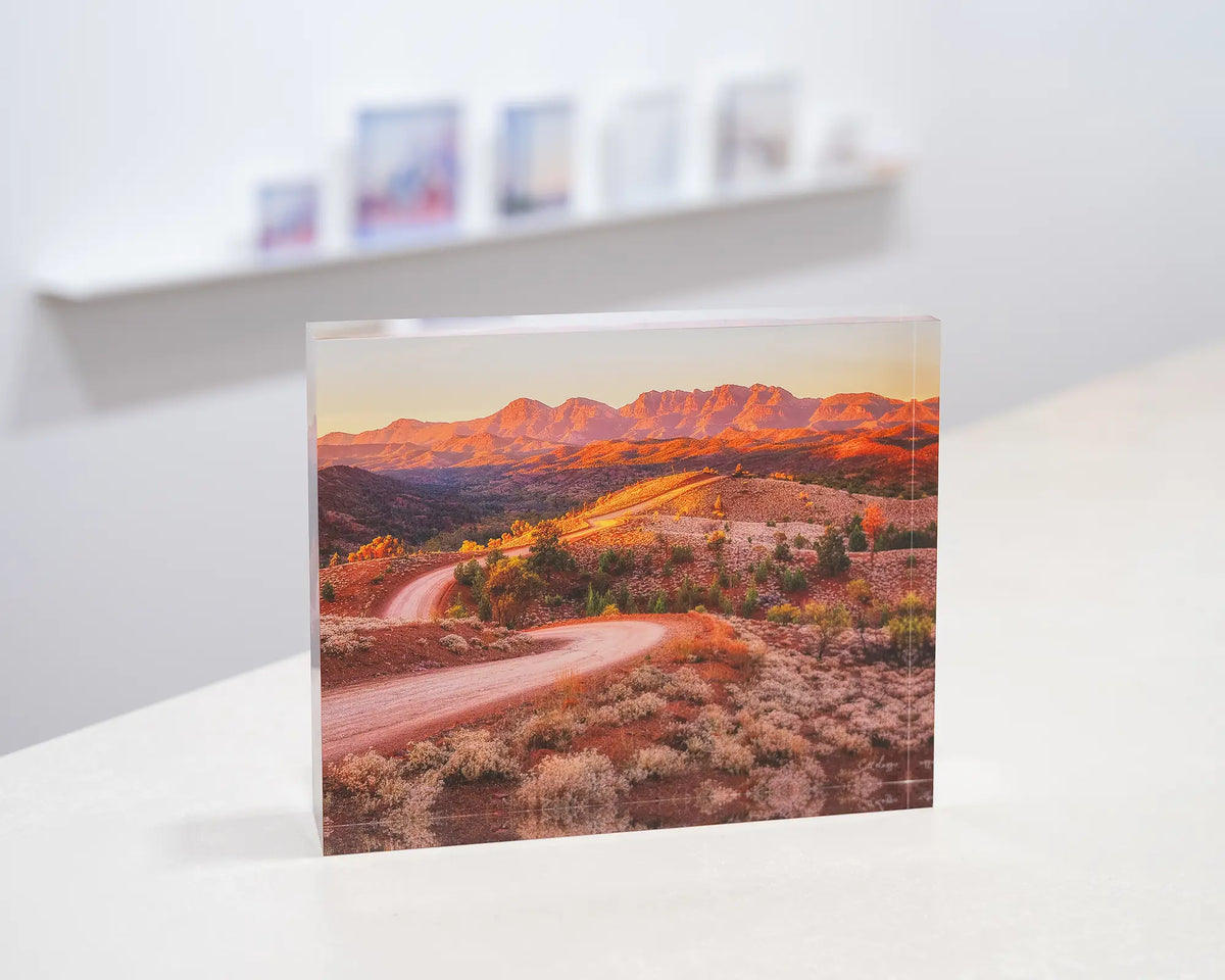 Razorback Ridge. Acrylic block of sunrise over Bunyeroo Valley and Wilpena Pound, South Australia, on gallery desk with acrylic blocks on shelf in background.