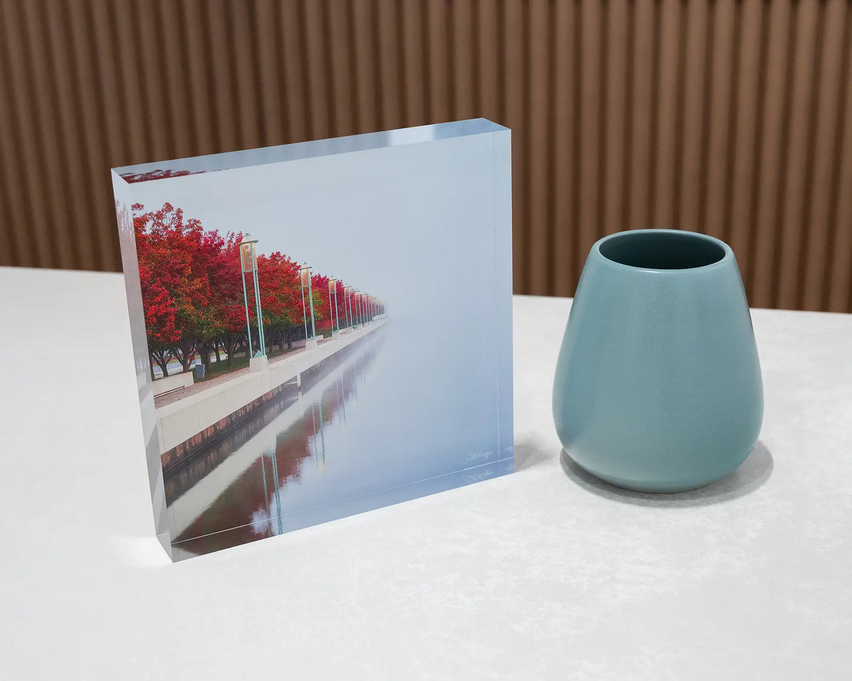 Red Serenity. Acrylic block of autumn trees lining Lake Burley Griffin, Canberra, on desk styled with a small vase.