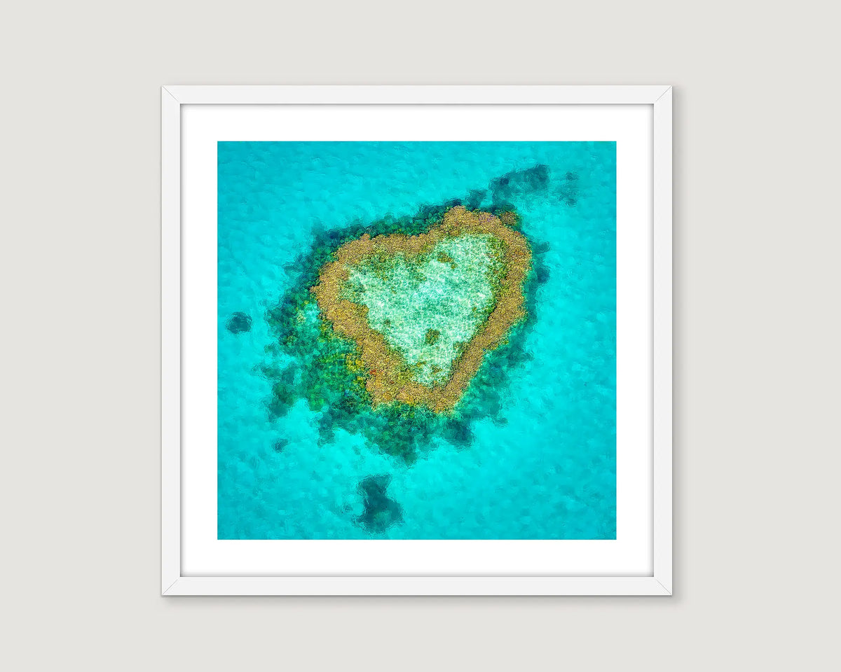 Framed photograph of a coral reef in the shape of a heart in turquoise water.