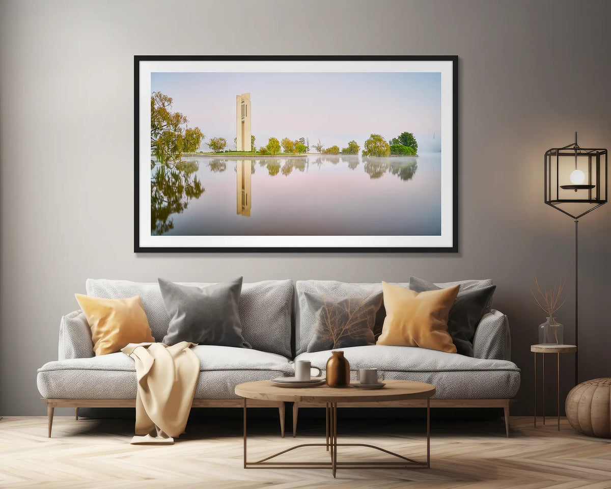 Reflective. Wall art print of early morning reflections at the National Carillon, Canberra, framed in a black frame, hung above a lounge seat. 