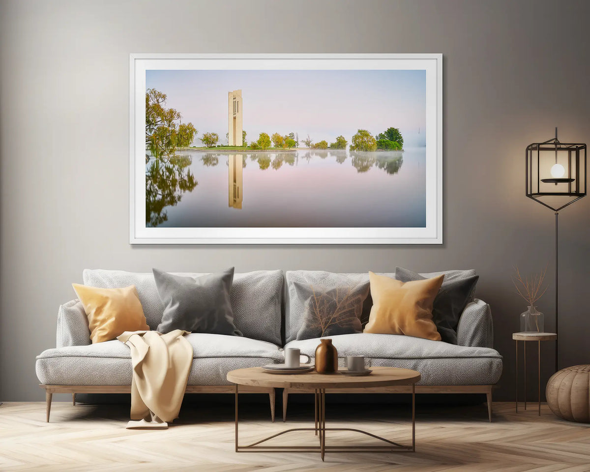 Reflective. Wall art print of early morning reflections at the National Carillon, Canberra, framed in a white frame, hung above a lounge seat. 