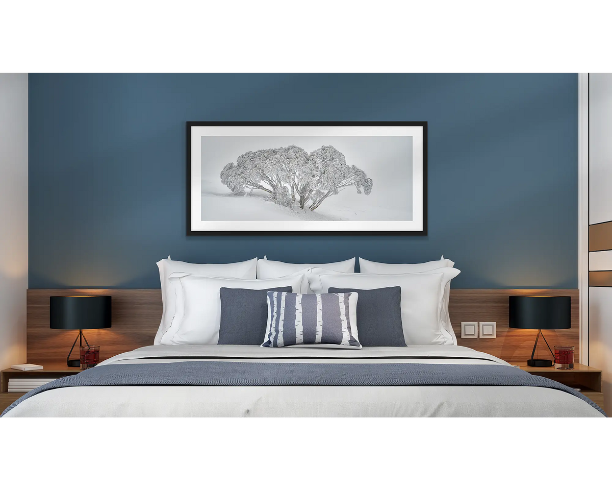 Revealed. Wall art print of a snow gum covered in snow,, framed with a black frame and hung above a bed in a hotel room. 