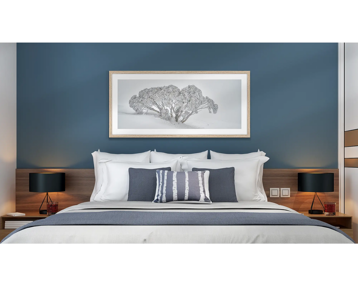 Revealed. Wall art print of a snow gum covered in snow,, framed with a timber frame and hung above a bed in a hotel room. 