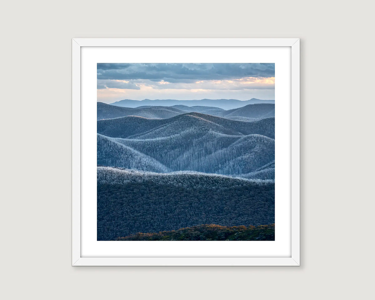 Framed neutral photograph of a mountainous region with forest and a blue grey cloudy sky in Alpine National Park.