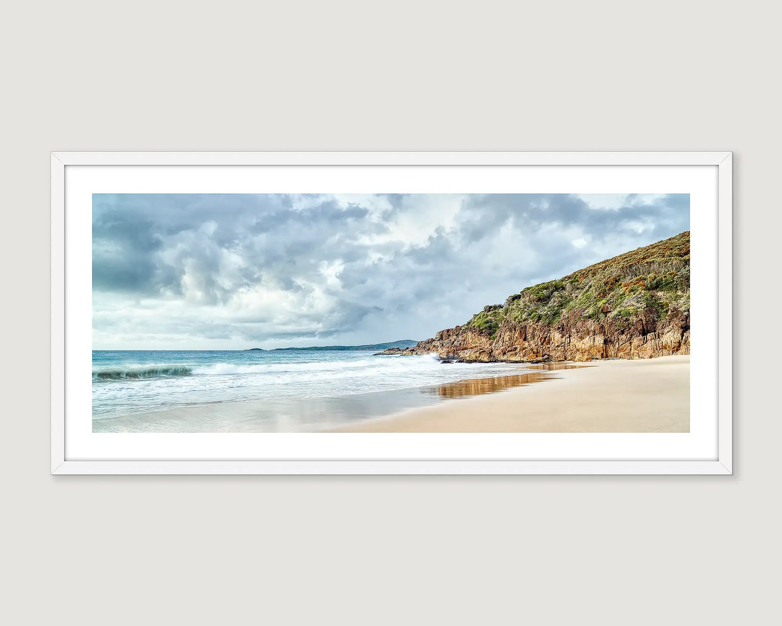 Framed artwork of a beach scene at Zenith Beach with a rocky cliff and cloudy sky.