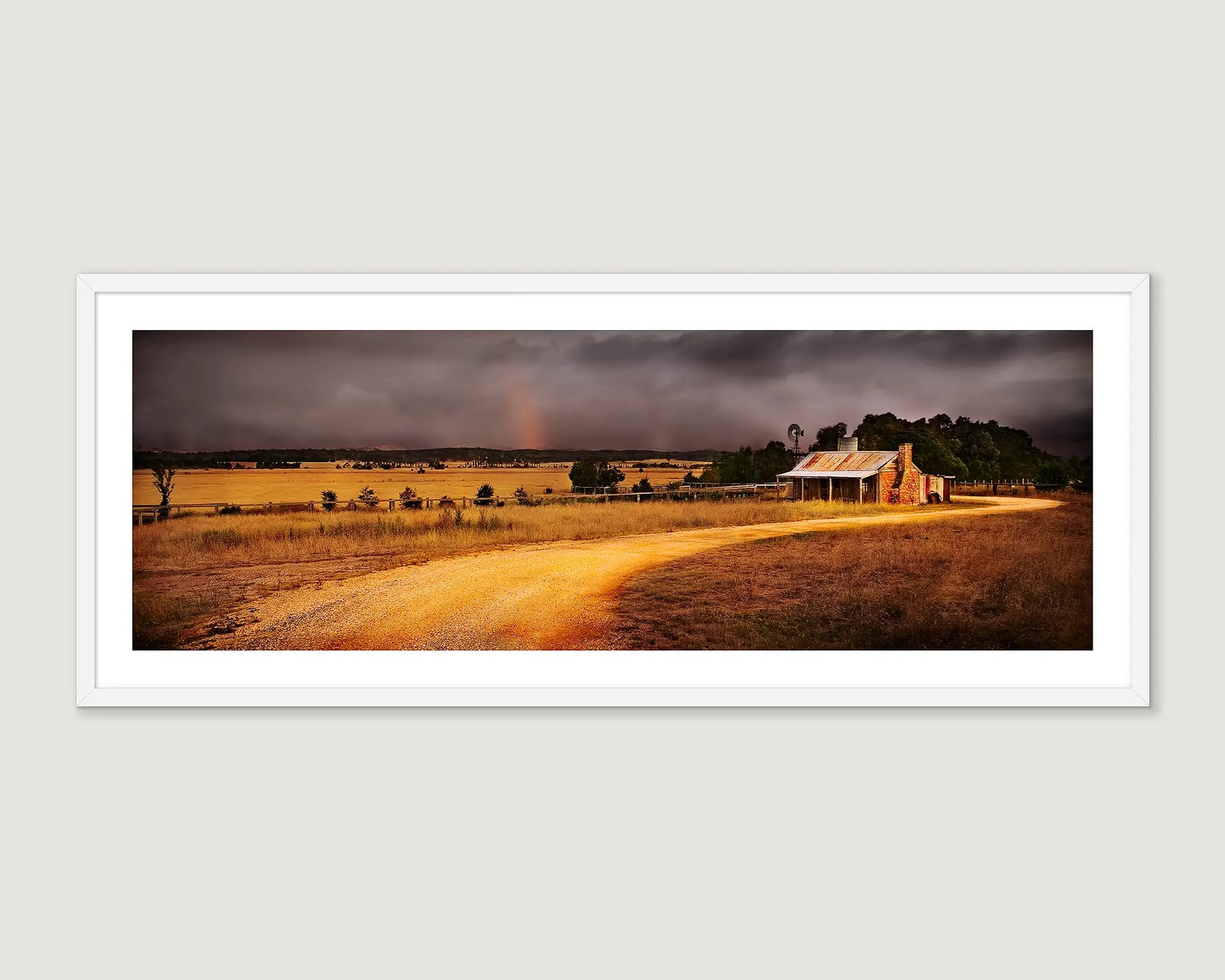 Framed panoramic landscape of a rural scene with a rainbow in a stormy sky over a field and house.