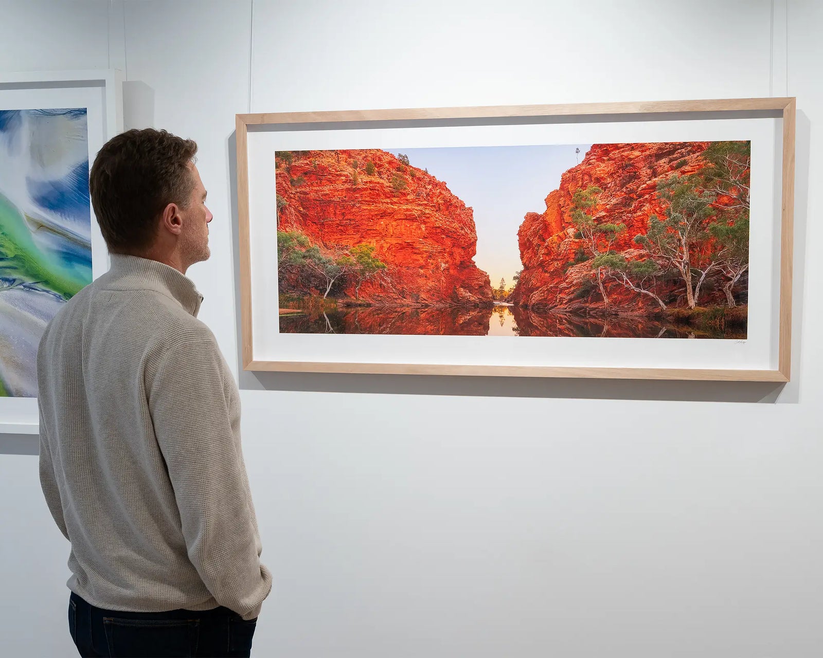 Framed photograph of a waterhole with large rocky cliffs and a blue sky.