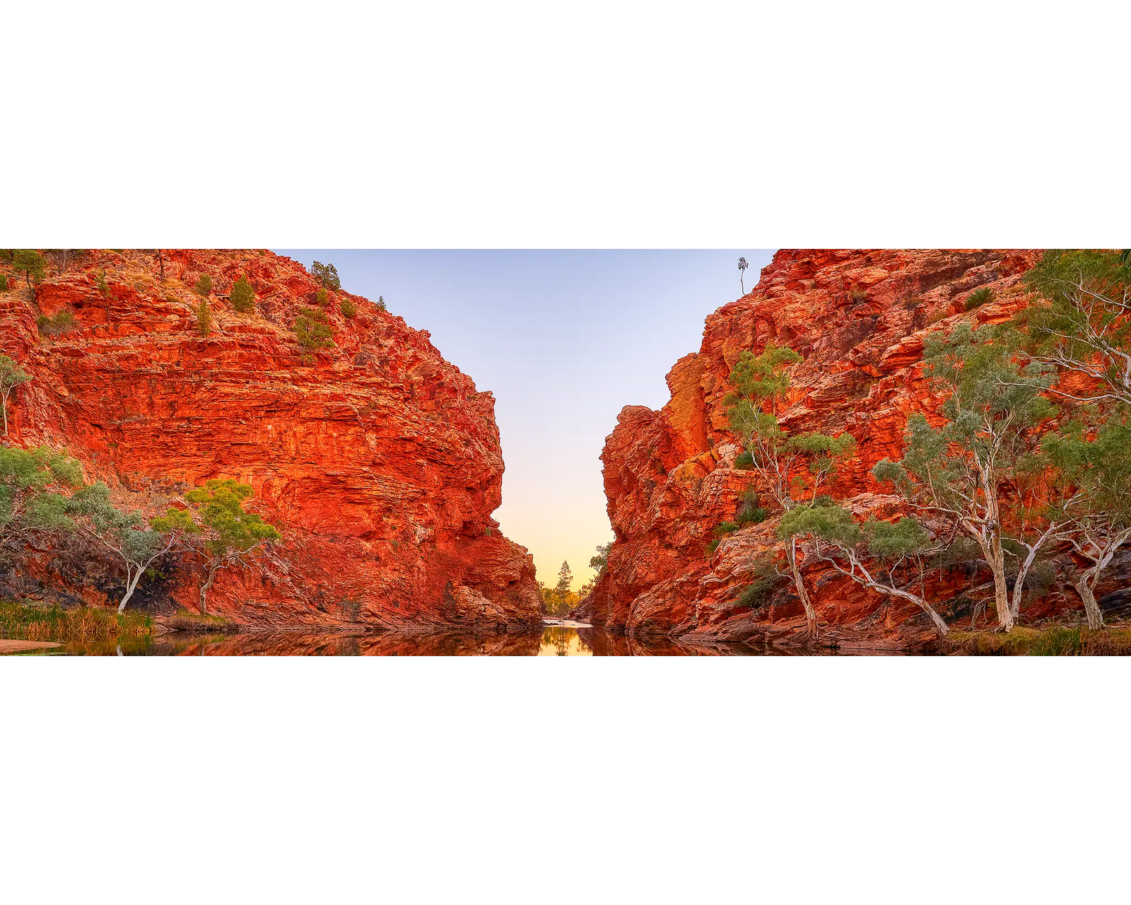 Red rock formation of Ellery Creek Big Hole with trees and a clear sky.