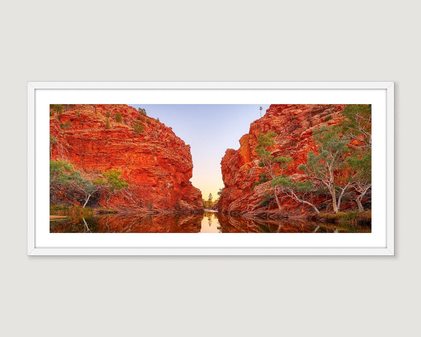 Framed photograph of a waterhole with large rocky cliffs and a blue sky.