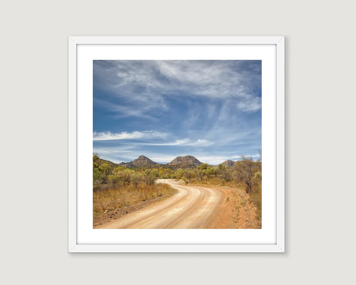 Framed print of a scenic dirt road with mountains and blue sky.