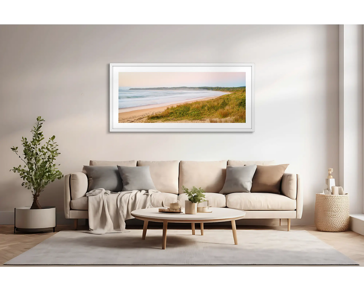 Seaside Dawn. Wall art print of a sunrise at Durras Beach, with a white frame, hung above a lounge room couch. 
