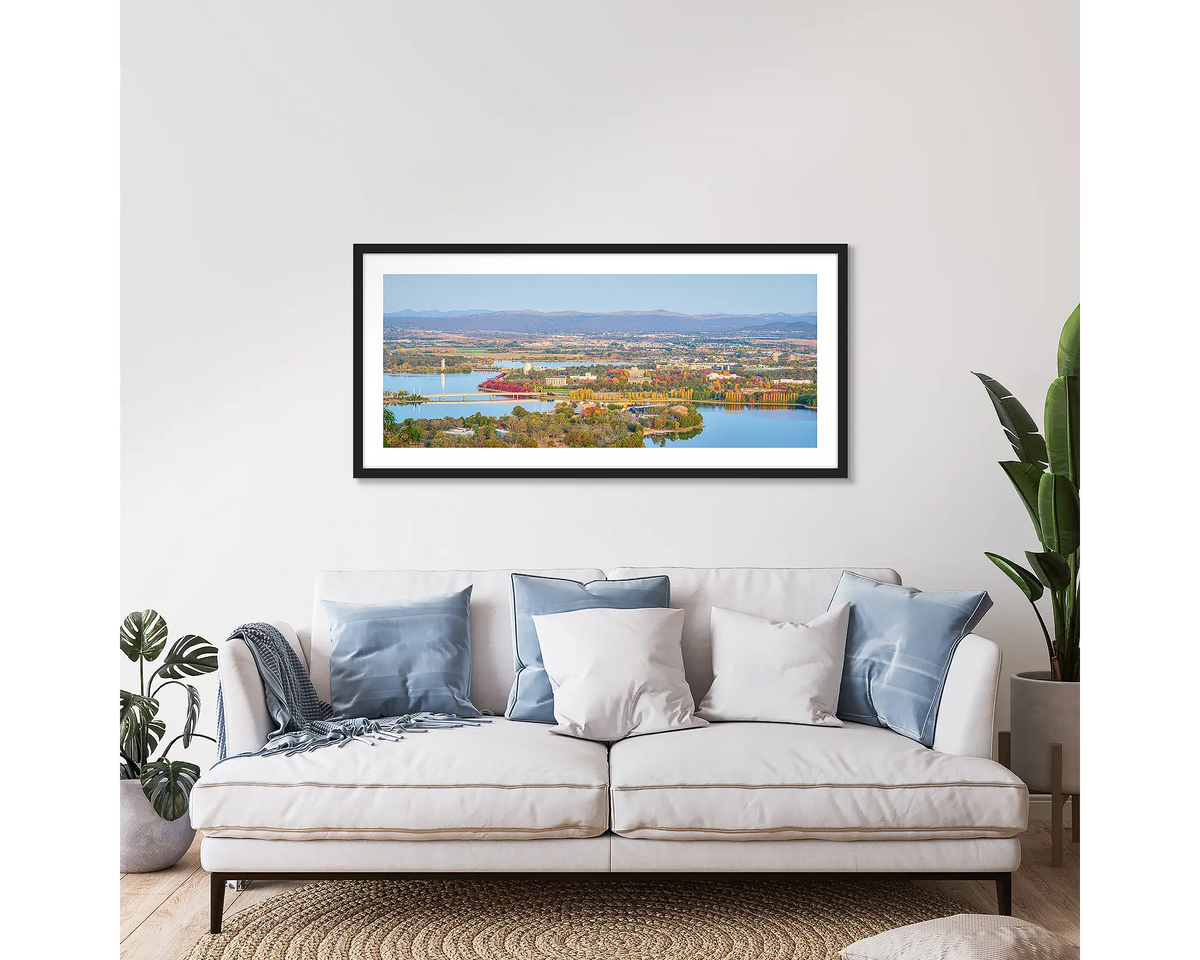 Seasonal Views. Framed wall art print of Canberra in autumn, with a black frame, hung above a couch. 