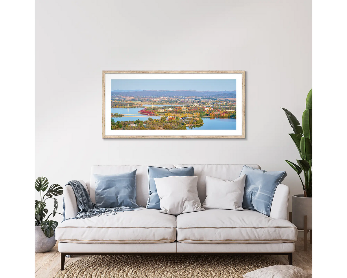 Seasonal Views. Framed wall art print of Canberra in autumn, with a timber frame, hung above a couch. 