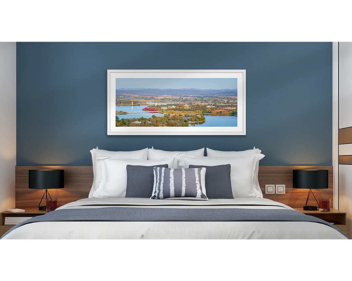 Seasonal Views. Wall art print of an Autumn sunset over Canberra, framed with a white frame and hung above a bed in a hotel room. 