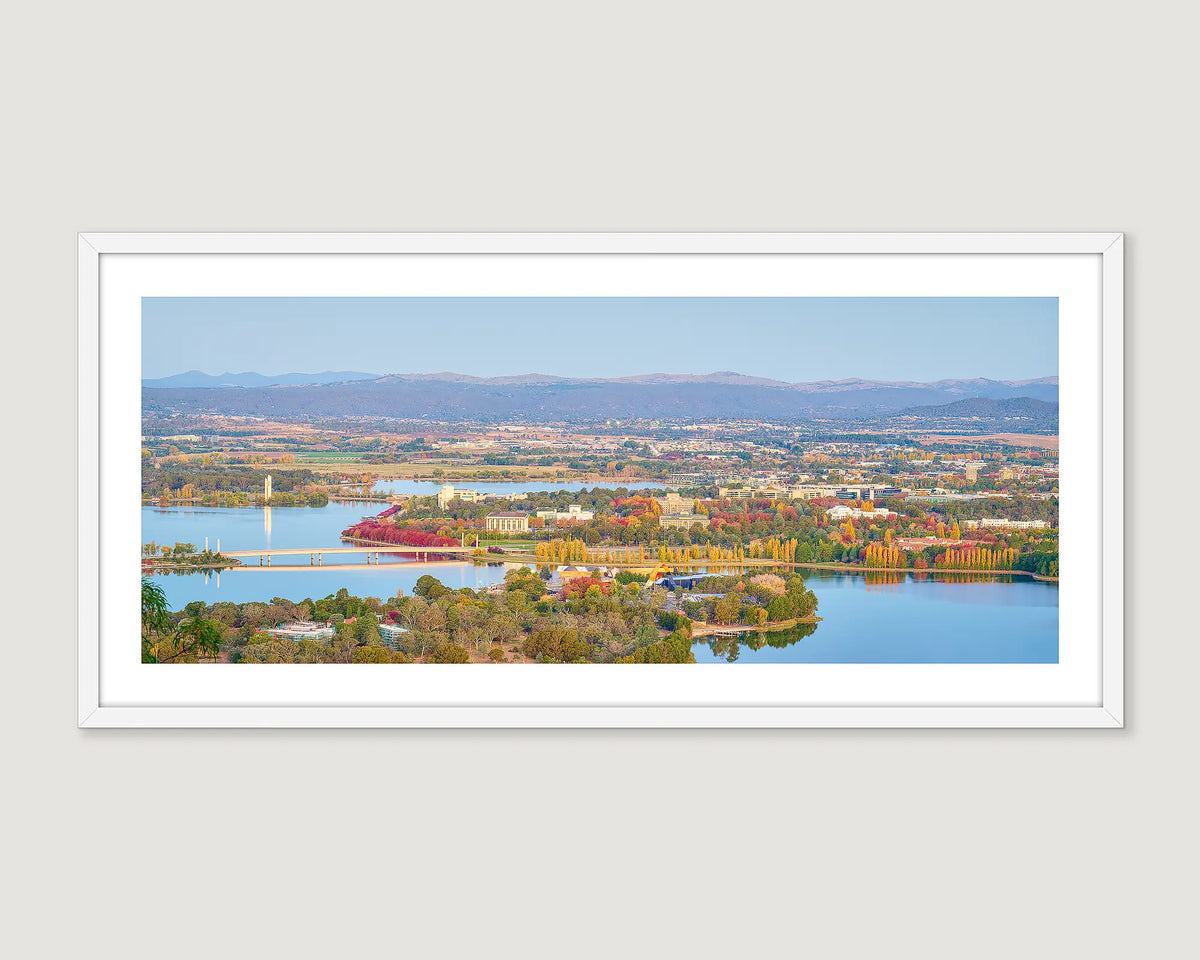 Framed panoramic view of a Canberra cityscape with a lake, trees and a mountain range.