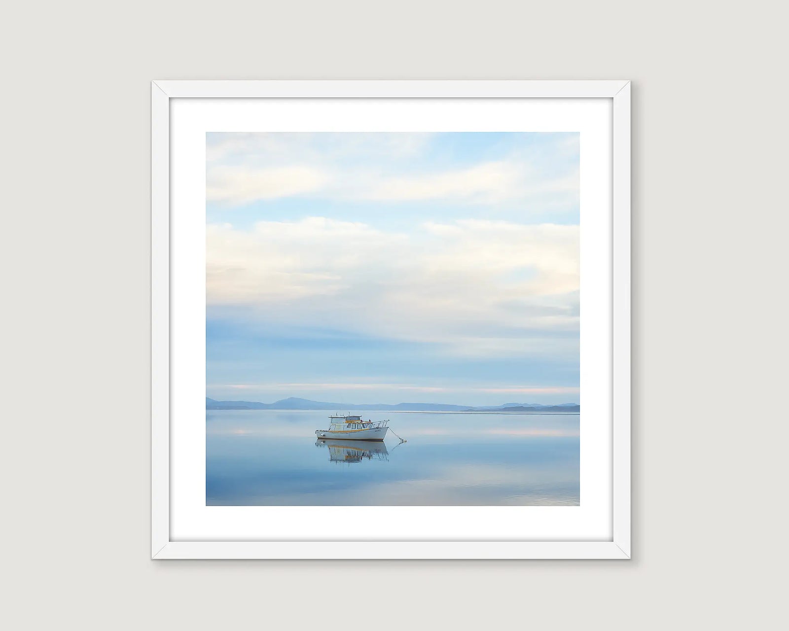 Framed artwork of a boat on a calm Macquarie Harbour with a cloudy sky and mountains.