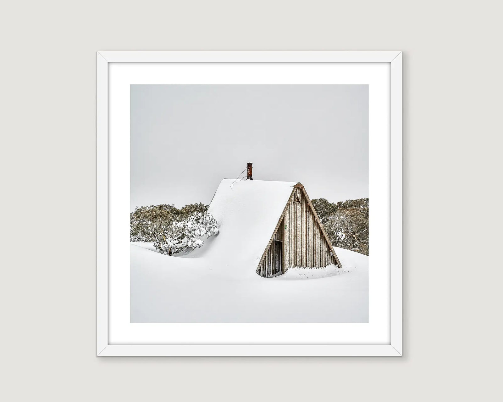 Framed photograph of a snow-covered A-frame Diamantina Hut in a forest.