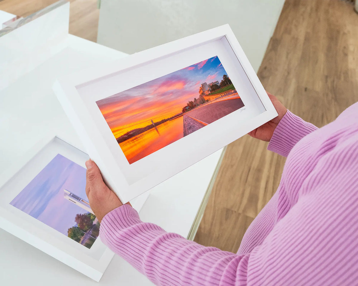 Sky Light. Small print with white frame of sunrise over Lake Burley Griffin, Canberra, held in hands.