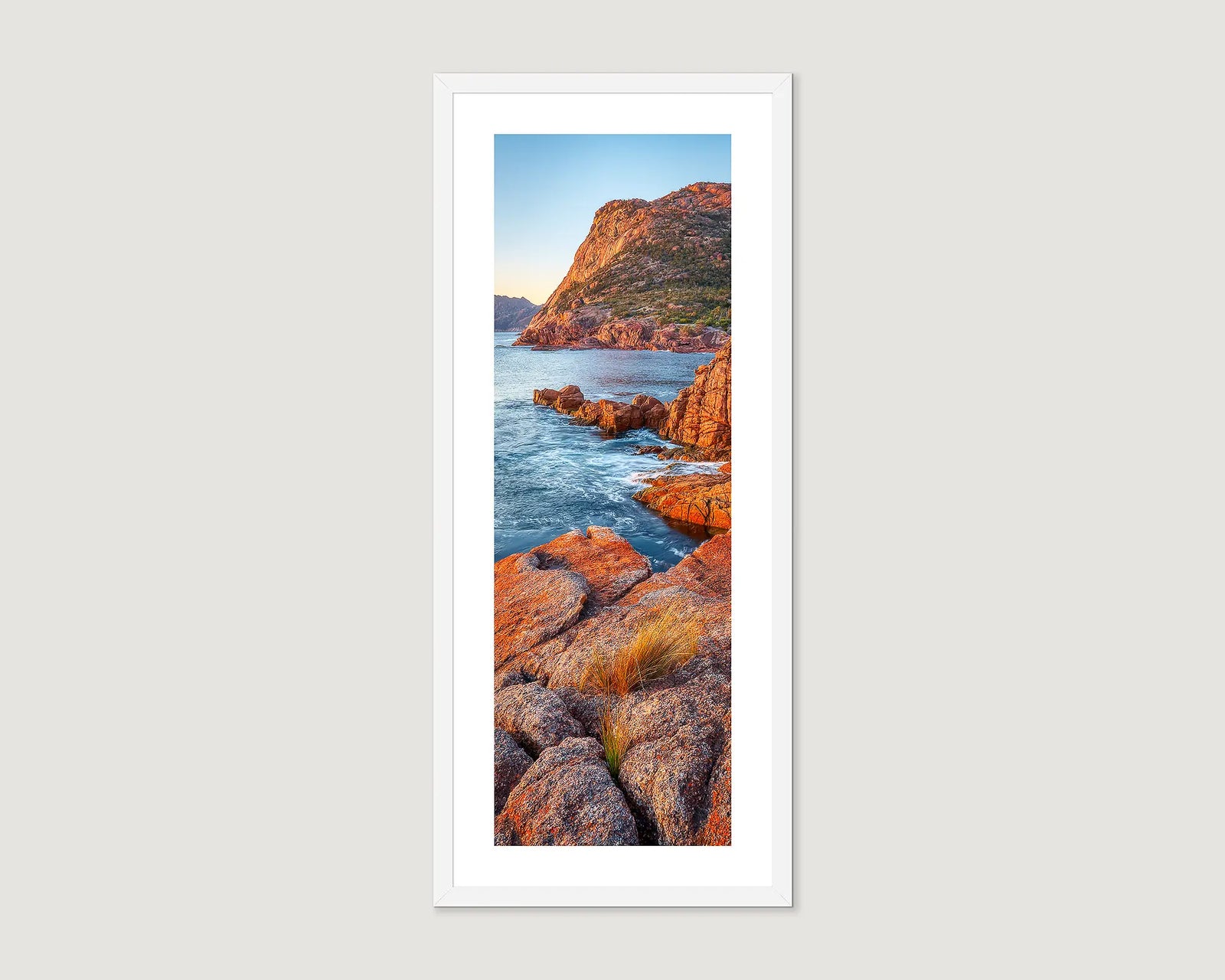 Framed artwork of a coastal scene with rocky cliffs and blue water at sunrise.