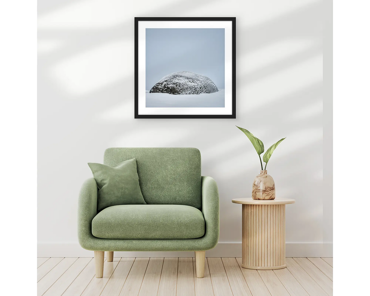 Snow Dome. Framed wall art print of a rock covered in ice with a black frame, hung above a one seat couch. 