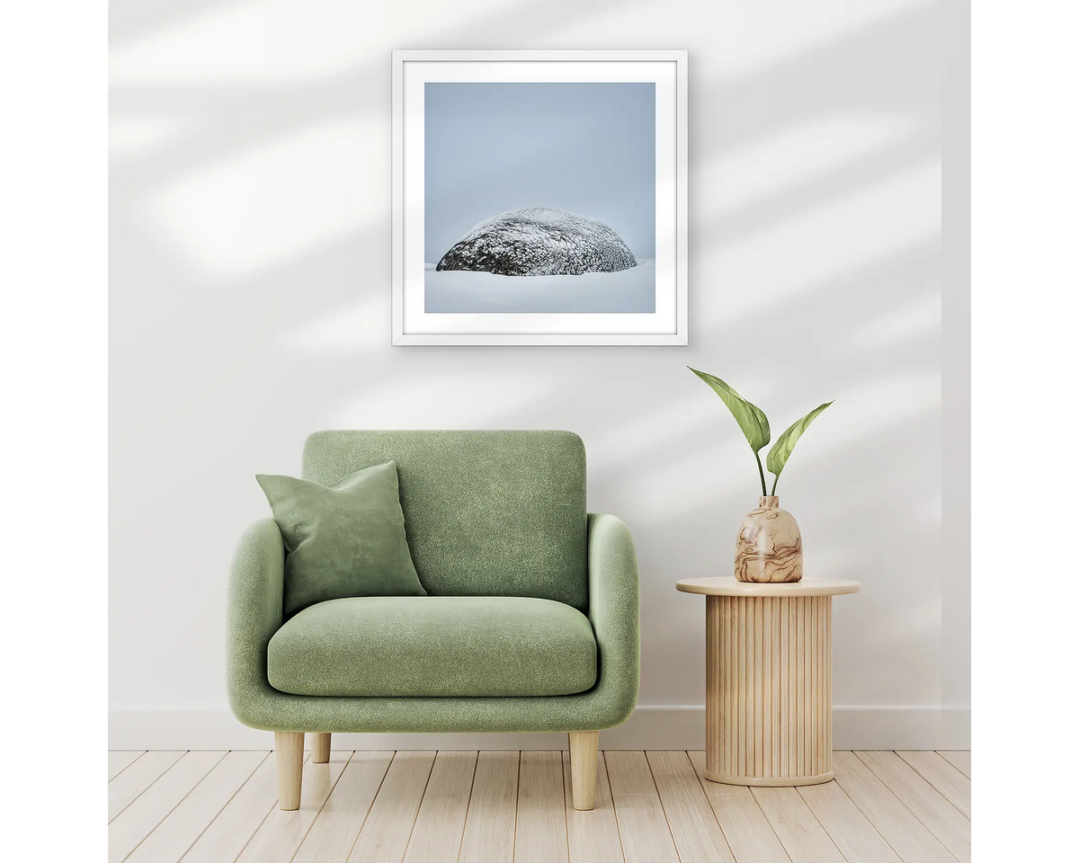 Snow Dome. Framed wall art print of a rock covered in ice with a white frame, hung above a one seat couch. 