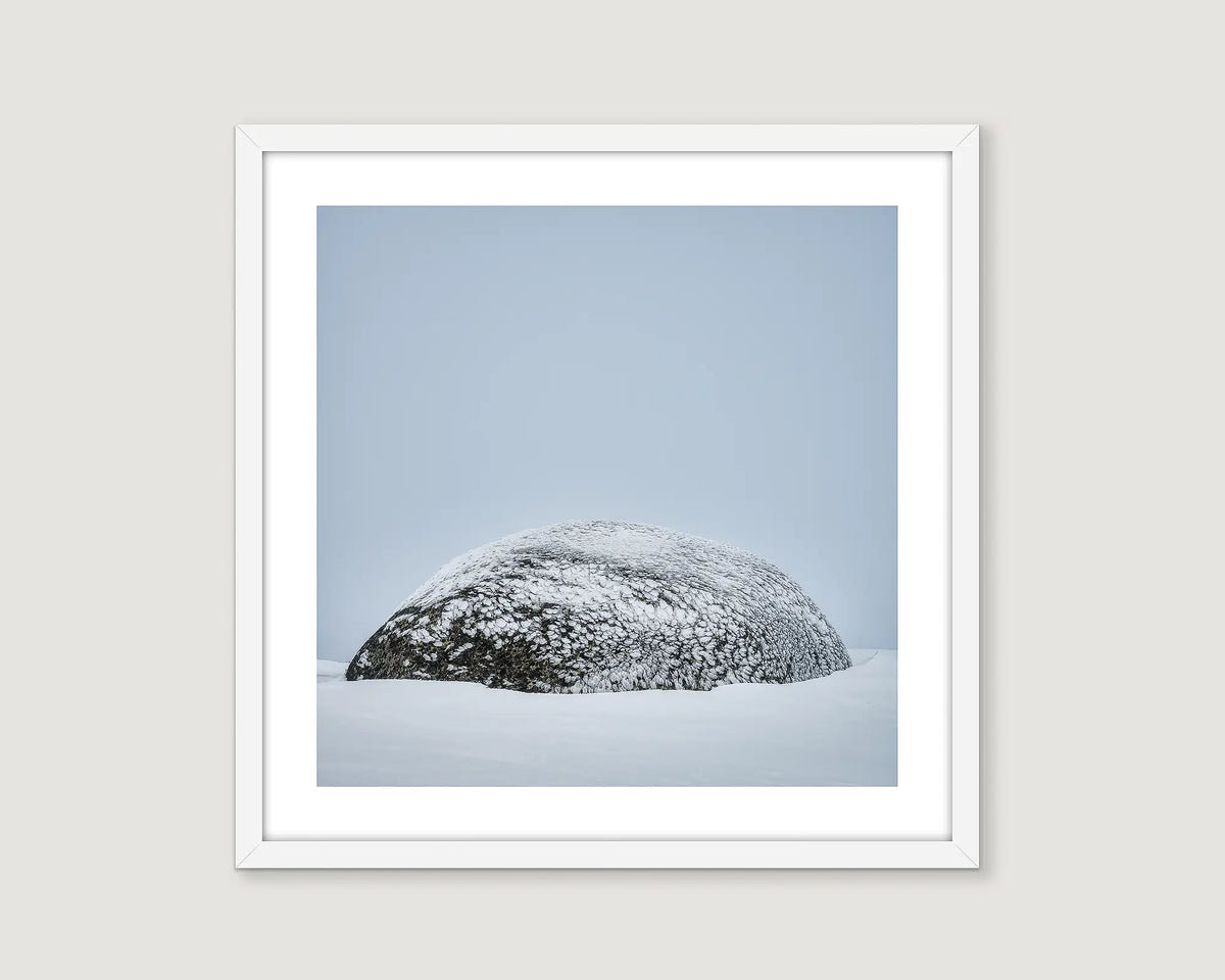 Framed photograph of a snow-covered rock against a light blue sky.