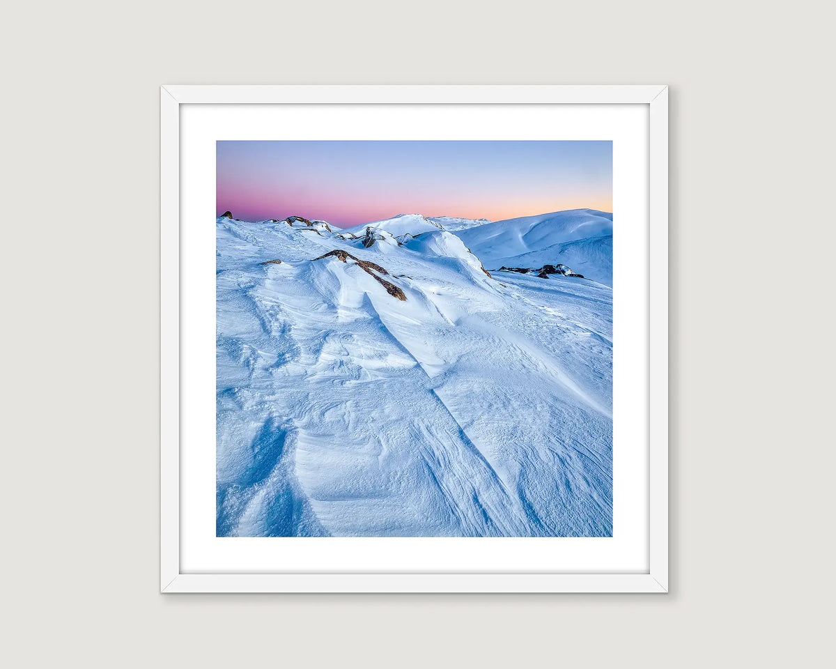 Framed photograph of snow covered mountains and a colourful sunrise and clear sky.