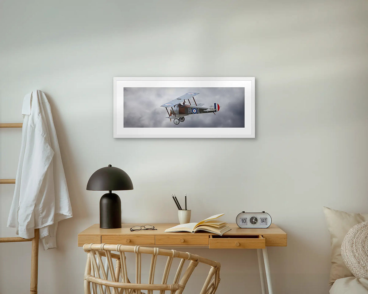 Sopwith Camel. Aviation wall art print, with a white frame, above a small desk.