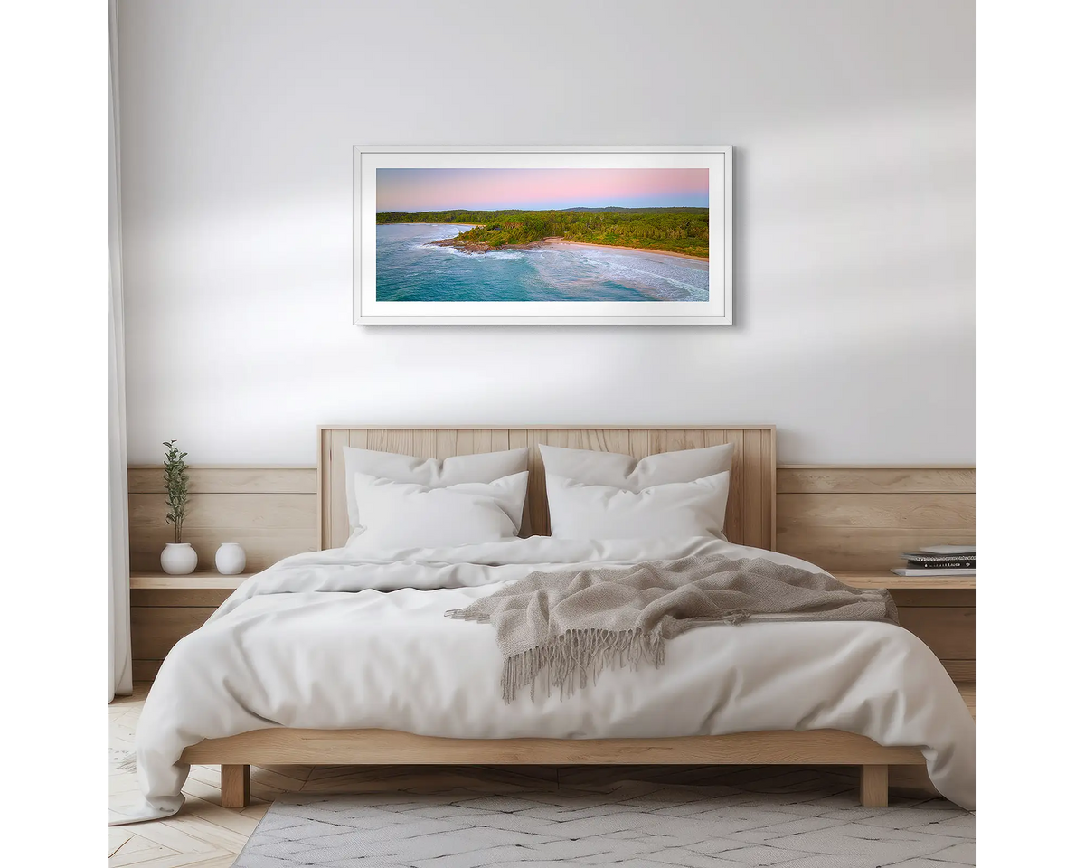 South Coast Escape. Wall art print of a sunrise over Durras, with a white frame hung above a bed. 