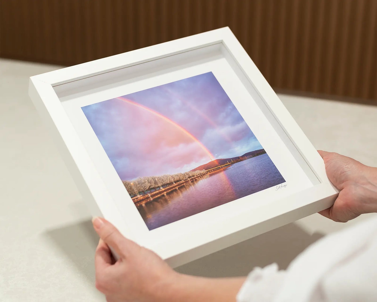 Framed photograph of a double rainbow over Lake Burley Griffin with trees and mountains in the background.