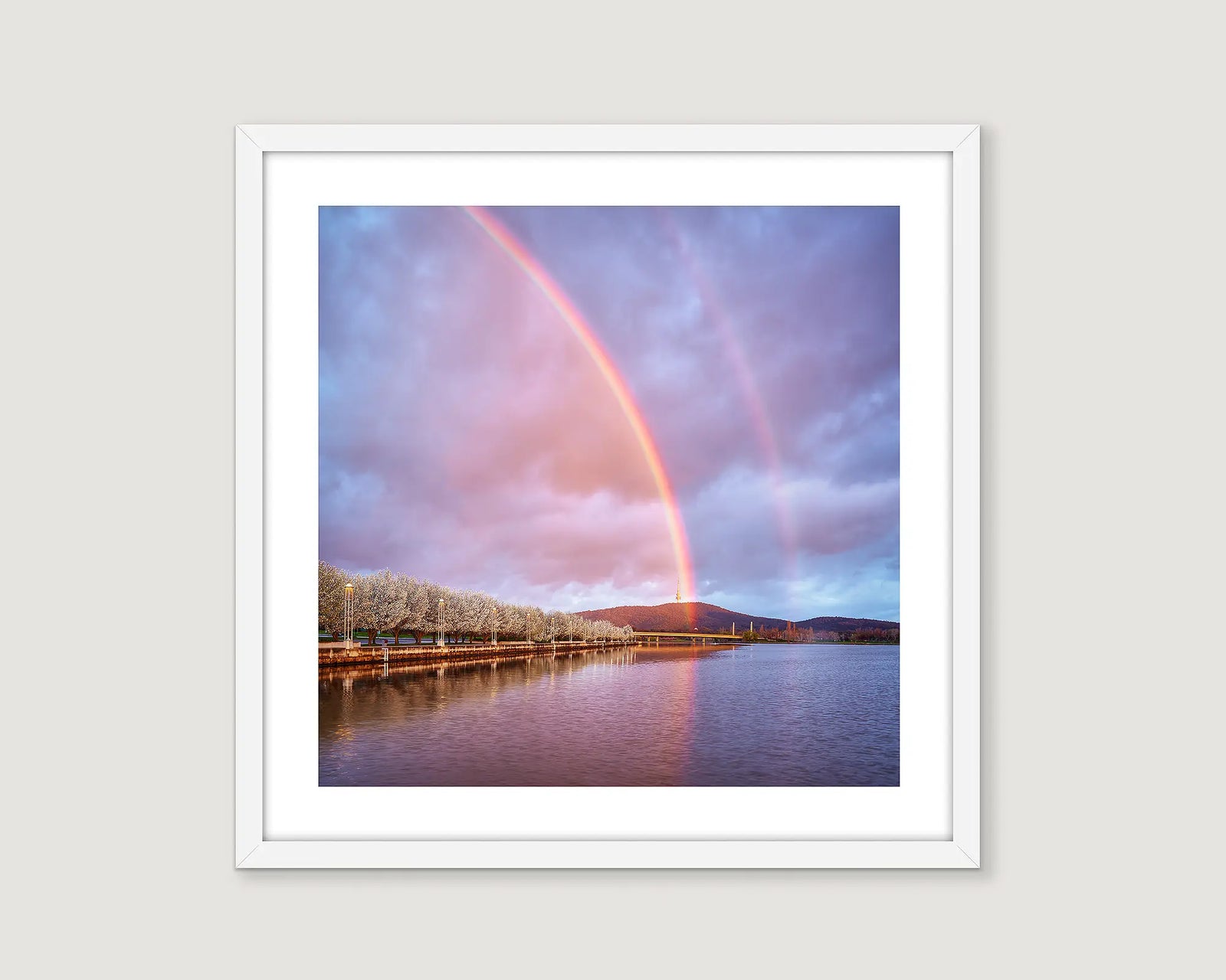 Framed photograph of a double rainbow over Lake Burley Griffin with trees and mountains in the background.