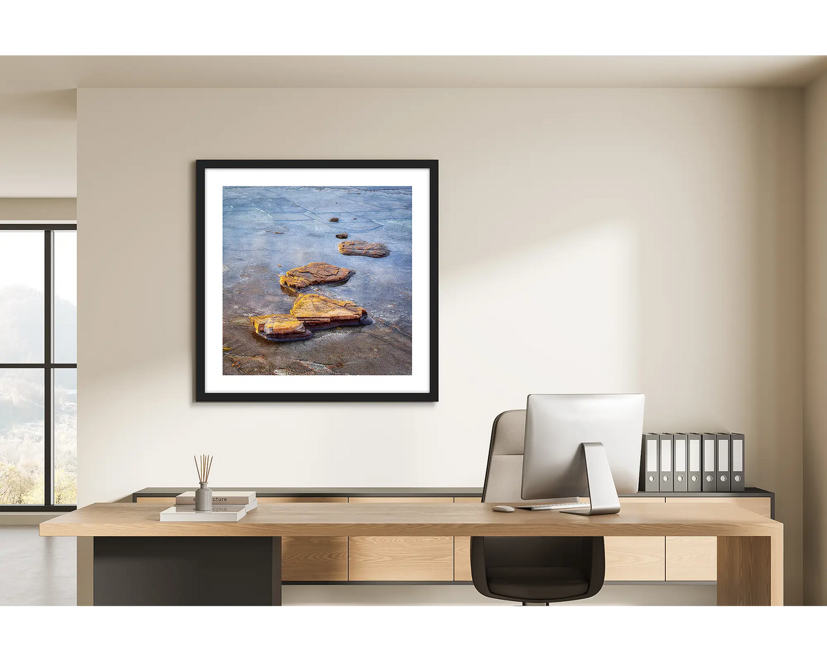 Stepping Stones. Coastal rocks, wall art print in a black frame hung behind a study desk. 