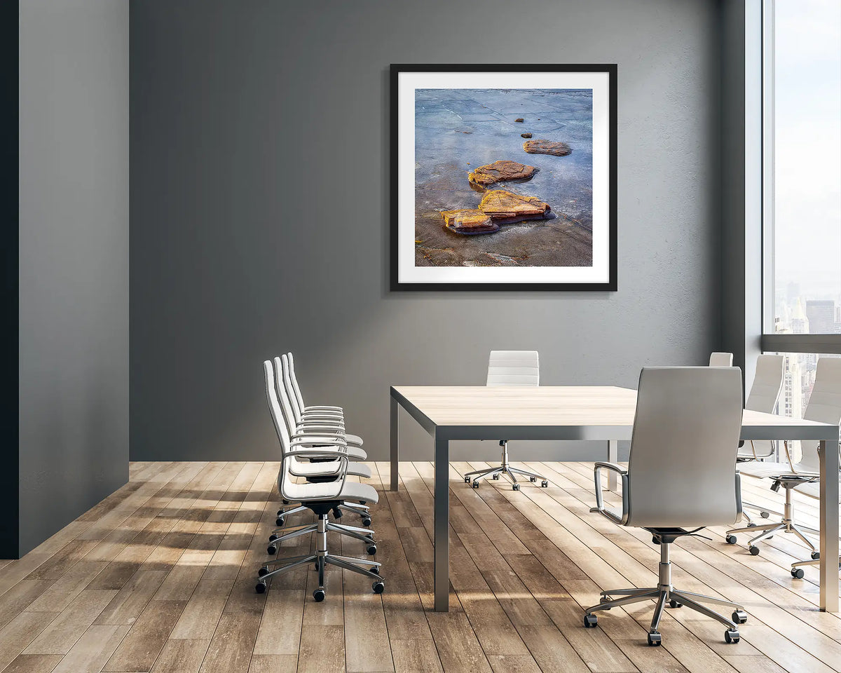 Stepping Stones. Coastal rocks, wall art print in a black frame hung in an office meeting room. 