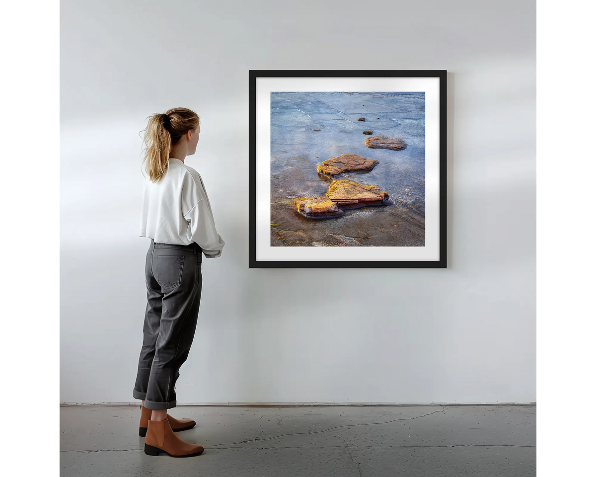 Stepping Stones. Coastal rocks, wall art print in a black frame with a person admiring. 
