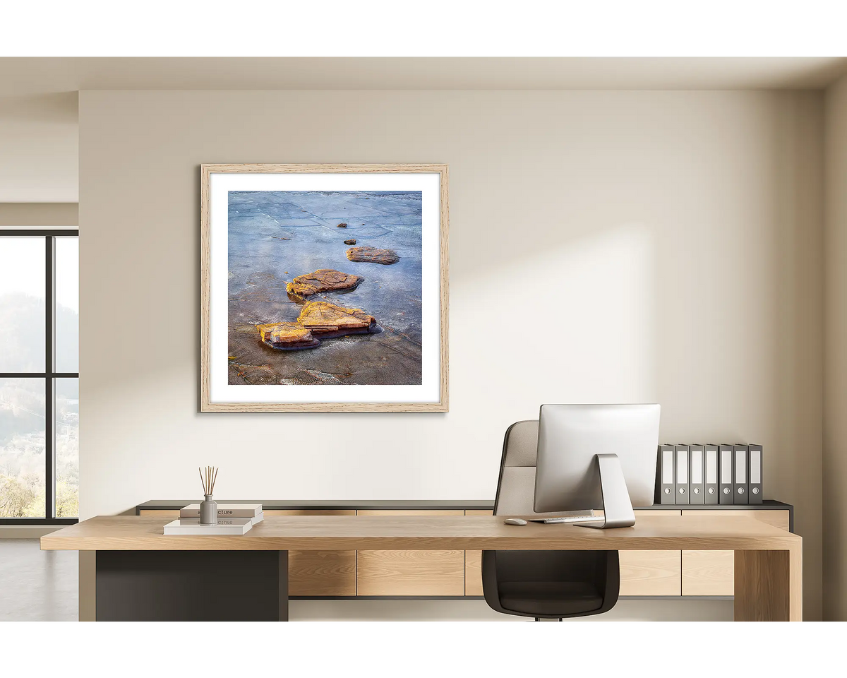 Stepping Stones. Coastal rocks, wall art print in a timber frame hung behind a study desk. 