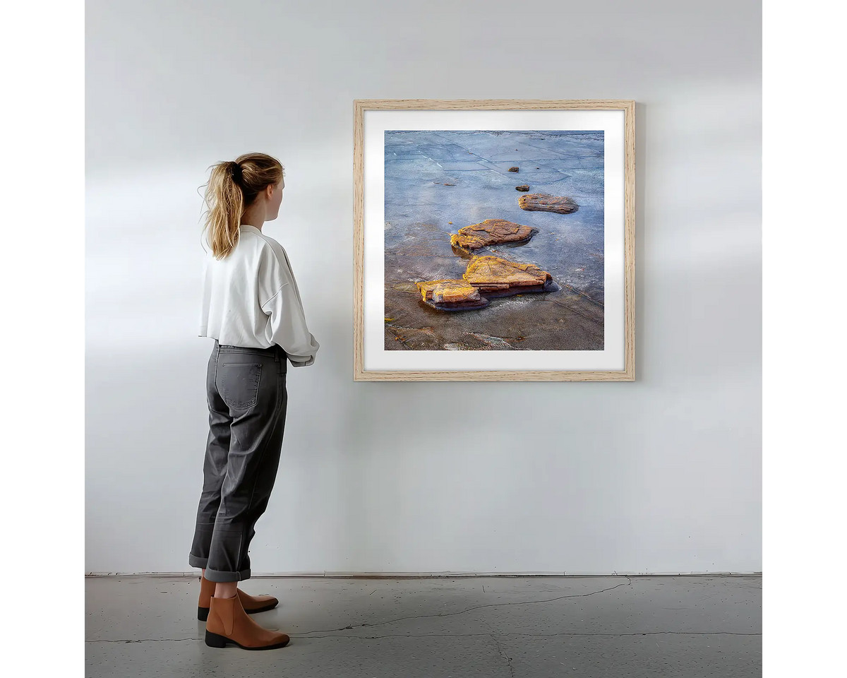 Stepping Stones. Coastal rocks, wall art print in a timber frame with a person admiring. 
