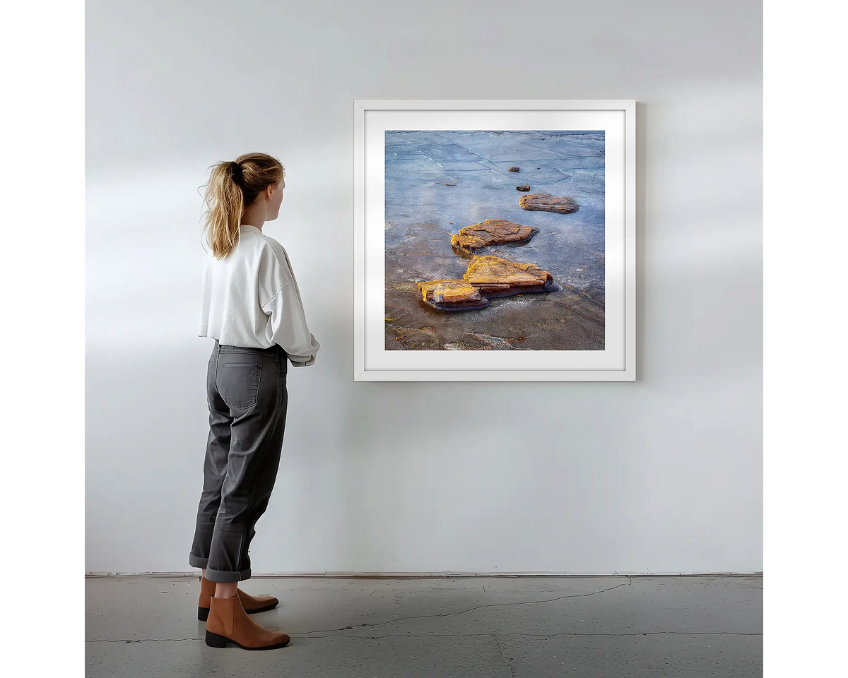 Stepping Stones. Coastal rocks, wall art print in a white frame with a person admiring. 