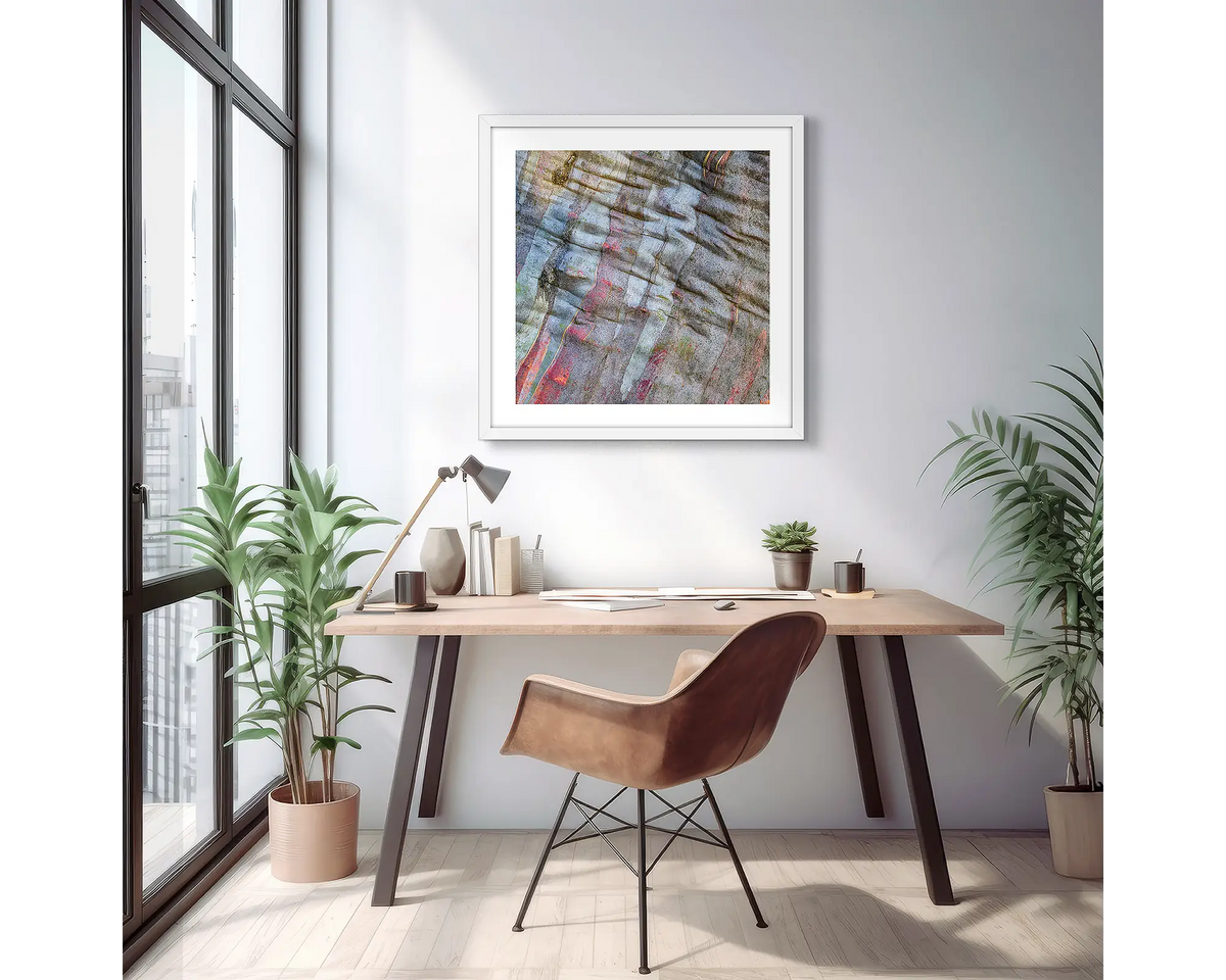 Stirling Colours. Abstract wall art print of colours in snow gum bark, with a white frame, hung on an apartment wall above a small desk.